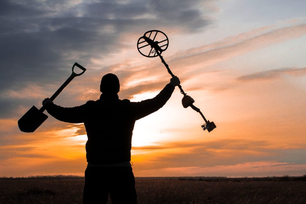 treasure hunter with a metal detector on a beveled wheat field in search of adventure against the backlight of the sun