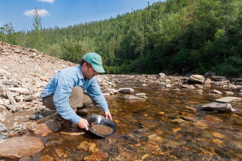 A visitor crouches in a shallow rocky creek panning gravel in a gold pan at a blm public gold panning area. Learn how to pan for gold.