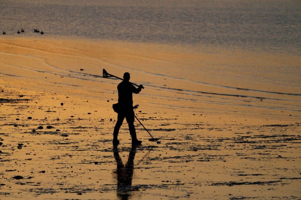 Best Metal Detectors For Christmas 2026: Tom’s Picks By Budget 3 Silhouette of a person metal detecting on wet beach sand
