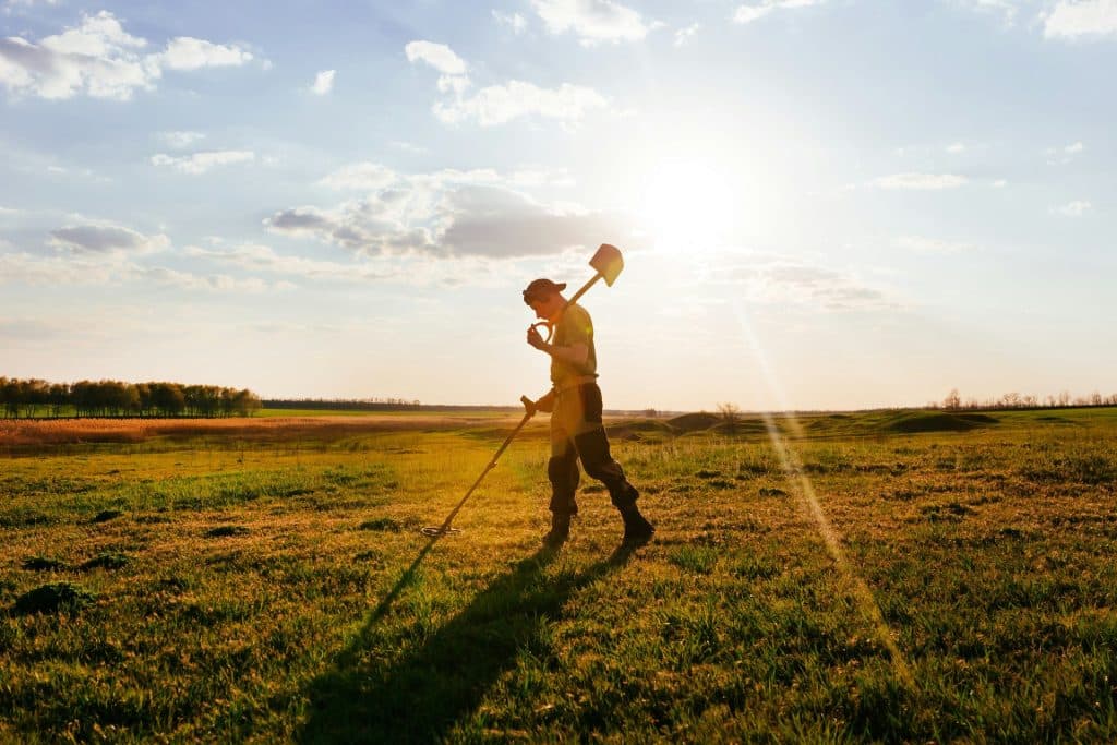 Best Metal Detectors For Christmas 2026: Tom’s Picks By Budget 6 Detectorist with headphones swinging a metal detector over a grassy field at sunset